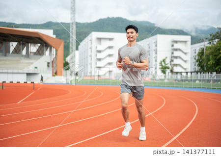 Asian athletic man running or jogging on a track lane in sports stadium. 141377111