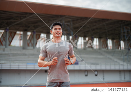 Smiling Asian male runner jogging running on track at sports stadium. 141377121
