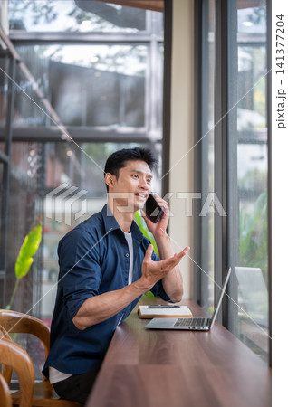 Young Asian entrepreneur talking on smartphone in modern cafe workspace 141377204
