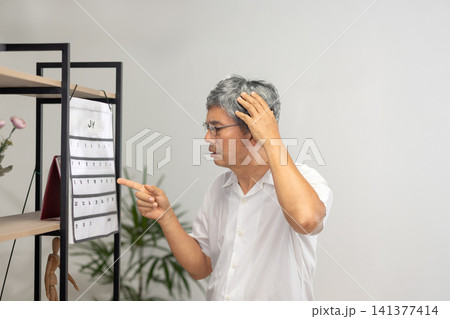 Senior Asian man with dementia struggles to set the time and day on his watch. Senior Asian man with dementia struggles to set the time and day on his watch. 141377414