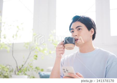 スマートフォンを操作する日本人男性 コーヒーを飲みながら情報を確認する在宅ライフスタイル スマートフォンを操作する日本人男性 コーヒーを飲みながら情報を確認する在宅ライフスタイル 141378170
