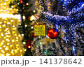 Close up red ball and golden present box hanging on pine tree branch with blurry warm yellow bokeh background for christmas celebration 141378642