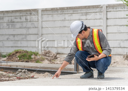 Engineer inspecting concrete surface at construction site while using tablet safety equipment for quality control structural assessment project supervision Engineer inspecting concrete surface at construction site while using tablet safety equipment for quality control structural assessment project supervision 141379534