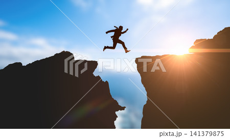 Businessman silhouette jumping across mountain gap during bright sunrise representing corporate risk extreme challenge ultimate success overcoming business obstacles achieving goals Businessman silhouette jumping across mountain gap during bright sunrise representing corporate risk extreme challenge ultimate success overcoming business obstacles achieving goals 141379875