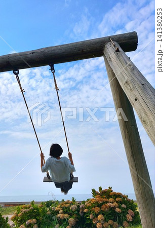 紫陽花が咲き海の見える砂浜でブランコに乗って遊ぶ女の子の後ろ姿 紫陽花が咲き海の見える砂浜でブランコに乗って遊ぶ女の子の後ろ姿 141380253