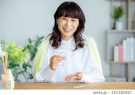 リビングで薬を飲む笑顔のミドル女性 リビングで薬を飲む笑顔のミドル女性 141380497
