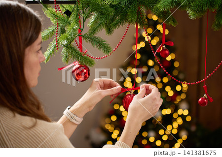 Woman decorating room for Christmas, hanging ornaments on pine garland at home. 141381675