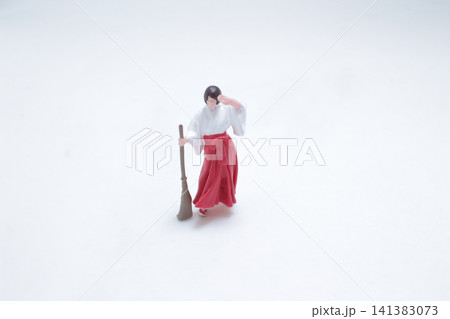 Miniature Shinto shrine maiden holds a sweeping broom. 141383073