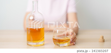 woman with glass of whiskey on table, suffering from alcohol addiction and alcoholism concept. depicting emotional distress, depression, substance abuse problem, unhealthy lifestyle and mental health 141383207