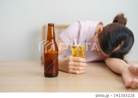 Stressed woman drinking beer alone with problem. Exhausted drunk woman looking stressed and sleepy. Alcohol addiction, Alcoholism, emotional distress and mental health concept 141383228
