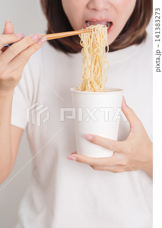 Happy young Asian woman enjoying a delicious cup of hot instant noodles while relaxing at home, Cheerful female eating instant ramen with a smile at apartment. Simple lifestyle and quick meal concept Happy young Asian woman enjoying a delicious cup of hot instant noodles while relaxing at home, Cheerful female eating instant ramen with a smile at apartment. Simple lifestyle and quick meal concept 141383273