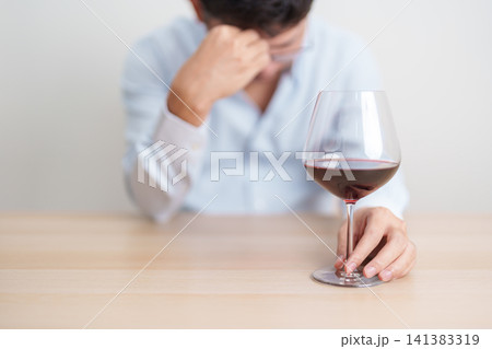 Stressed man drinking Wine alone with problem. Exhausted drunk man looking stressed and sleepy. Alcohol addiction, Alcoholism, emotional distress and mental health concept Stressed man drinking Wine alone with problem. Exhausted drunk man looking stressed and sleepy. Alcohol addiction, Alcoholism, emotional distress and mental health concept 141383319