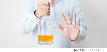 Man making stop hand gesture to refuse a bottle of whiskey, Healthy man say no to alcohol drink, stop alcoholism and addiction concept. Responsible man reject a drink before driving and quit booze 141383337