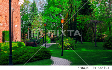 Idyllic landscaped garden path with ornate street lanterns and lush greenery 141385193
