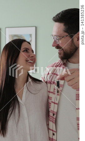Vertical video Happy couple owners of a new apartment show the key looking at the camera. Buying first family real estate, move in new home. Home buying. 141385236