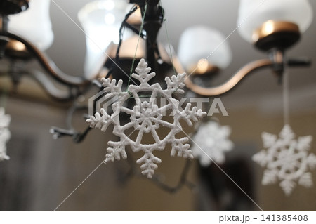 White frosted snowflake ornament adorns a metal chandelier in a living room for holiday cheer White frosted snowflake ornament adorns a metal chandelier in a living room for holiday cheer 141385408