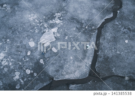 Close up view of a frozen surface featuring icy cracks and broken pieces of ice Close up view of a frozen surface featuring icy cracks and broken pieces of ice 141385538