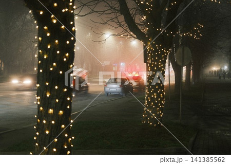 Foggy night street with illuminated trees and a car on fire 141385562