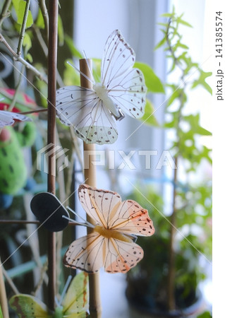 Two artificial butterflies on a bamboo stick among green houseplants Two artificial butterflies on a bamboo stick among green houseplants 141385574