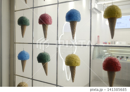 Decorative ice cream cones with colorful scoops hang inside a shop window. Decorative ice cream cones with colorful scoops hang inside a shop window. 141385685