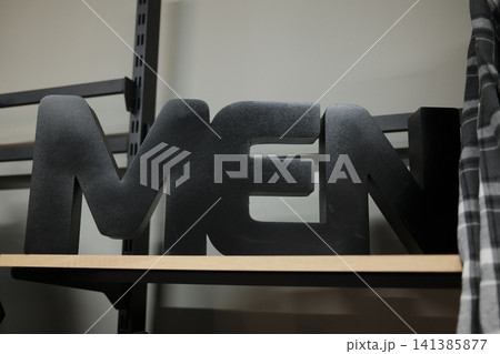 Black MEN sign on wood shelf in clothing store, plaid shirt to right Black MEN sign on wood shelf in clothing store, plaid shirt to right 141385877