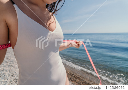 Weight loss fitness measurements woman in white swimsuit using pink tape on pebble beach to track body progress during summer Weight loss fitness measurements woman in white swimsuit using pink tape on pebble beach to track body progress during summer 141386061