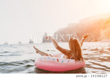 Woman, float, ocean. Relaxing woman on inflatable donut in open sea with rocky cliffs, enjoying summer leisure with copy space. Woman, float, ocean. Relaxing woman on inflatable donut in open sea with rocky cliffs, enjoying summer leisure with copy space. 141386127