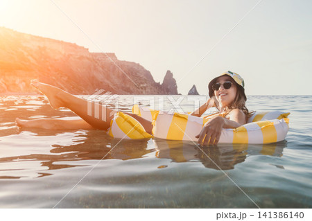 Woman, Beach, Float - Relaxing on a yellow and white striped inflatable float in the ocean near rocky cliffs. Woman, Beach, Float - Relaxing on a yellow and white striped inflatable float in the ocean near rocky cliffs. 141386140