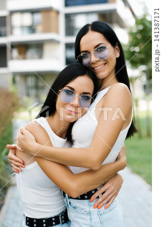 Twin Sisters Wearing Sunglasses Hugging Outdoors 141387171