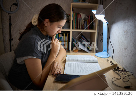 Teen girl studying by battery lamp during blackout 141389126