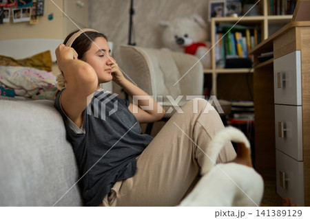 Teen girl relaxing with headphones and dog 141389129