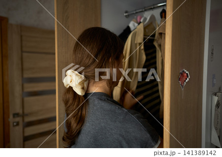 Teen girl searching clothes in open wardrobe Teen girl searching clothes in open wardrobe 141389142