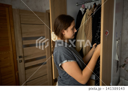 Teen girl searching clothes in open wardrobe Teen girl searching clothes in open wardrobe 141389143