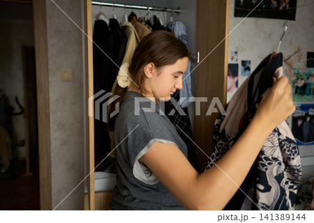 Teen girl searching clothes in open wardrobe Teen girl searching clothes in open wardrobe 141389144