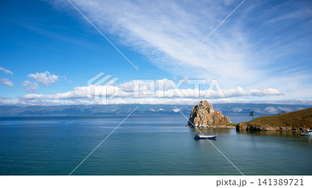 Wide landscape view of Olkhon island in Lake Baikal. Small blue boat on deep water with mountains in the background. Summer travel destination in Siberia, Russia Wide landscape view of Olkhon island in Lake Baikal. Small blue boat on deep water with mountains in the background. Summer travel destination in Siberia, Russia 141389721