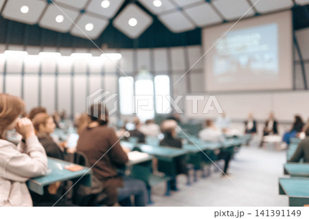 A large group of diverse people attending a professional presentation or educational workshop in a modern lecture hall. Defocus image of audience from behind. A large group of diverse people attending a professional presentation or educational workshop in a modern lecture hall. Defocus image of audience from behind. 141391149