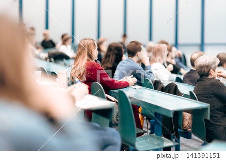 A large group of diverse people attending a professional presentation or educational workshop in a modern lecture hall. Focus on the audience from behind. 141391151