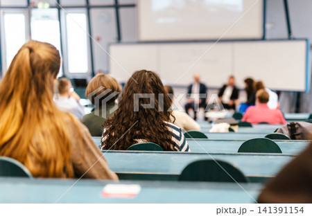 A large group of diverse people attending a professional presentation or educational workshop in a modern lecture hall. Focus on the audience from behind. 141391154