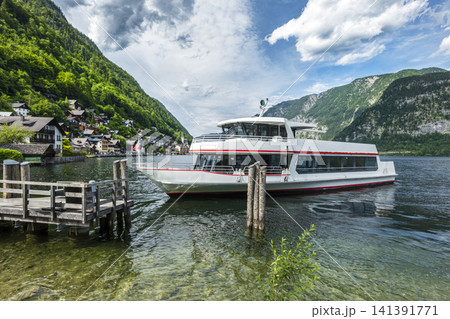 Passenger boat cruising on Lake Hallstatt with mountain landscape in Austria, illustrating scenic summer tourism in Europe. Passenger boat cruising on Lake Hallstatt with mountain landscape in Austria, illustrating scenic summer tourism in Europe. 141391771