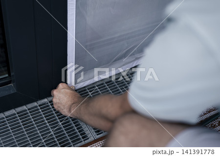 White mosquito screen being secured into the window frame, illustrating precise attachment in practical home maintenance. White mosquito screen being secured into the window frame, illustrating precise attachment in practical home maintenance. 141391778
