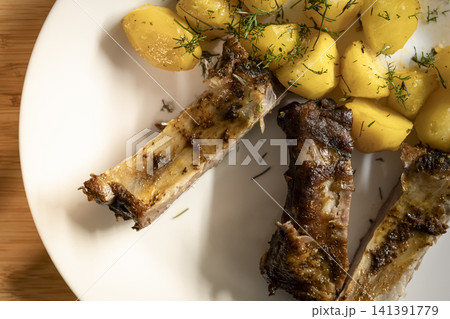 Barbecue ribs with potatoes and dill served on a wooden table, creating a home atmosphere with casual comfort food. Barbecue ribs with potatoes and dill served on a wooden table, creating a home atmosphere with casual comfort food. 141391779