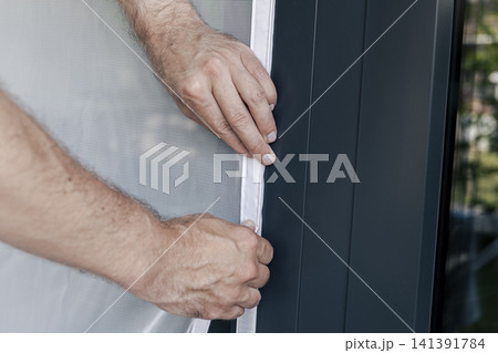 Hands adjusting a mosquito screen on a window frame, illustrating DIY home improvement for comfort and better living conditions. Hands adjusting a mosquito screen on a window frame, illustrating DIY home improvement for comfort and better living conditions. 141391784
