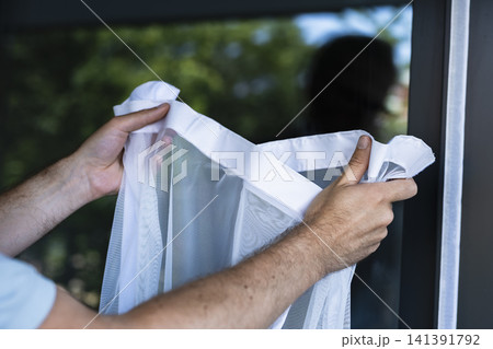 Person holding a white mosquito mesh near a window, illustrating an efficient home solution for daily protection from mosquitoes. Person holding a white mosquito mesh near a window, illustrating an efficient home solution for daily protection from mosquitoes. 141391792