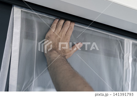 Hand securing a white mosquito screen into the window frame, illustrating precise handwork in home tasks and maintenance. Hand securing a white mosquito screen into the window frame, illustrating precise handwork in home tasks and maintenance. 141391793