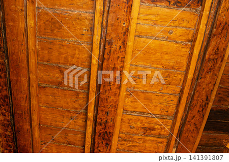 Detailed view of weathered wooden ceiling panels with rich orange and brown tones, showcasing natural wood texture and aged patina 141391807
