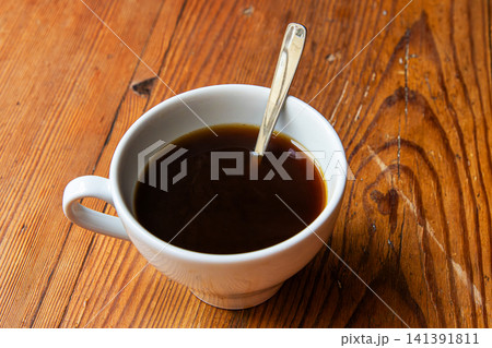 Minimalist top view of a white coffee cup with etal spoon placed on a textured wooden table or windowsill surface. Minimalist top view of a white coffee cup with etal spoon placed on a textured wooden table or windowsill surface. 141391811
