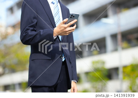 屋外でスマホを持つ20代のビジネスマン 141391939