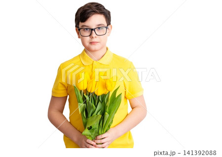 A boy in glasses and a yellow T-shirt holds a bouquet of yellow tulips A boy in glasses and a yellow T-shirt holds a bouquet of yellow tulips 141392088