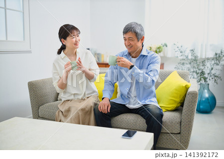 ソファに座ってコーヒーを飲む笑顔の60代の夫婦 ソファに座ってコーヒーを飲む笑顔の60代の夫婦 141392172