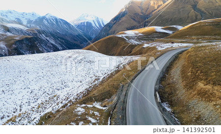 Aerial view of a winding asphalt road highway pass through snow covered mountain peaks and slopes in Georgia Caucasus region during late autumn travel journey Aerial view of a winding asphalt road highway pass through snow covered mountain peaks and slopes in Georgia Caucasus region during late autumn travel journey 141392501